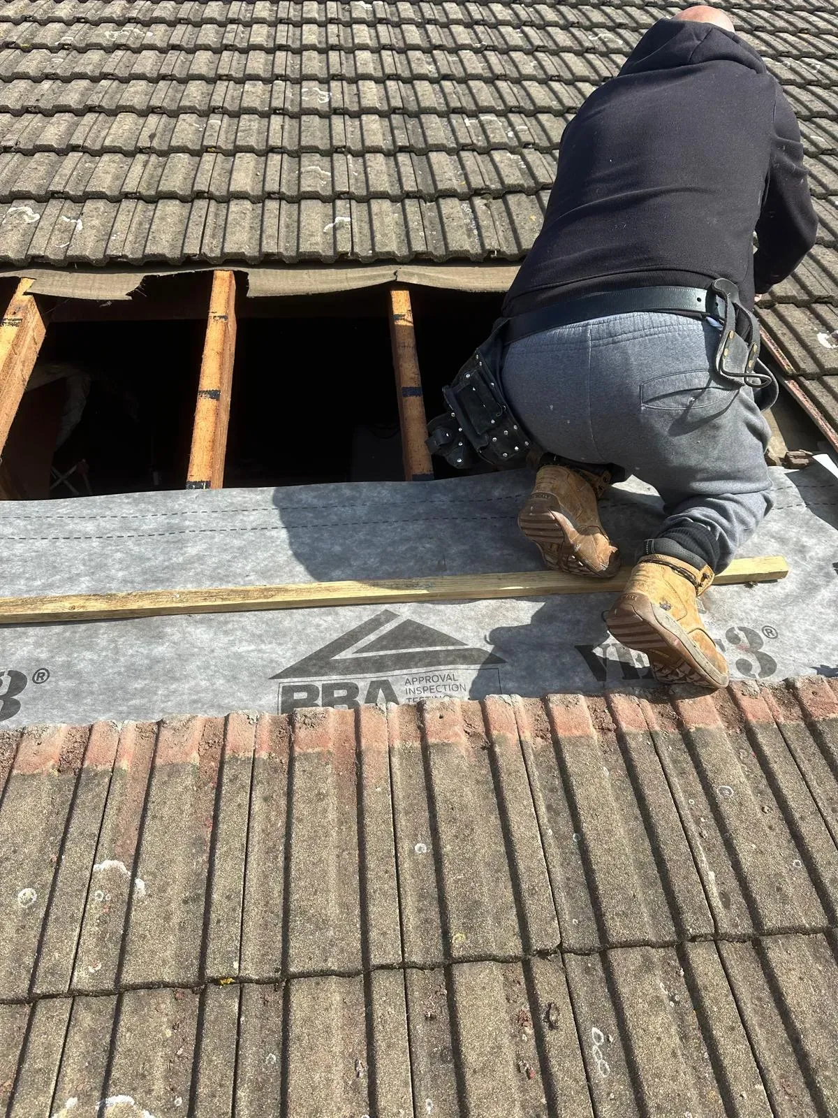 Professional roofer repairing a tiled roof in West Malling, Kent, installing new roofing underlay and battens.