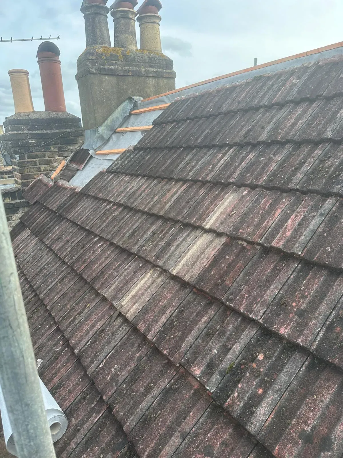 Professional roof tile repairs in progress showing new battens and lead flashing next to a chimney.